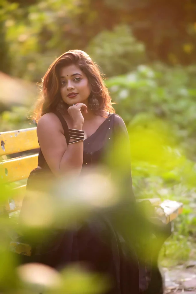 Woman wearing a black saree, with silver earrings and black bangles, posing outdoors with a serene and confident expression.