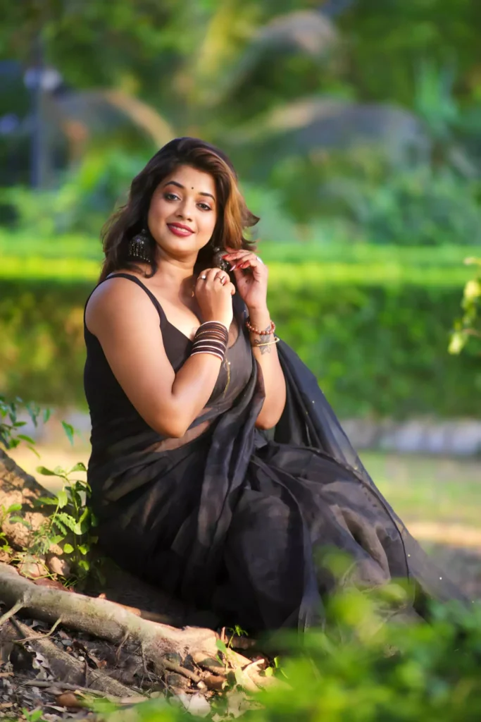 Woman wearing a black saree, with silver earrings and black bangles, posing outdoors with a serene and confident expression.