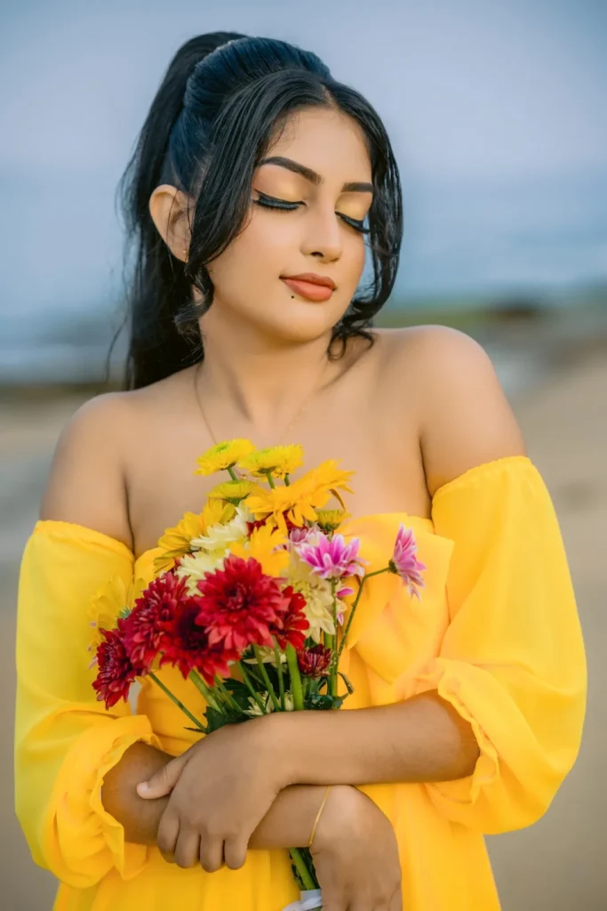 A beautiful young woman in a yellow dress holds a colourful bouquet of flowers, showcasing her beauty.