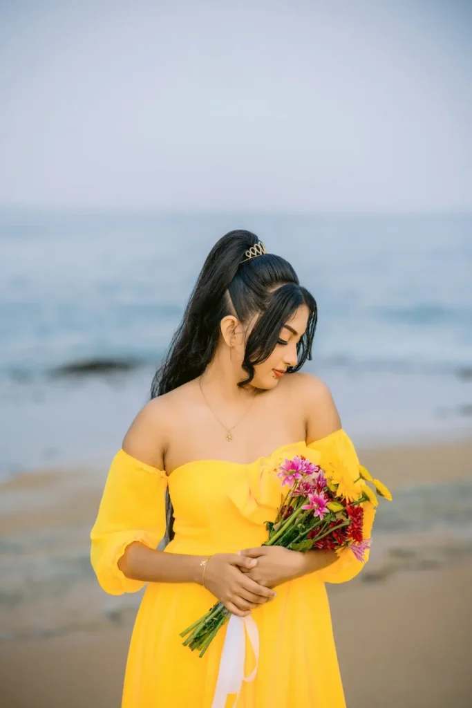 A beautiful young woman in a yellow dress holds a colourful bouquet of flowers, showcasing her beauty.