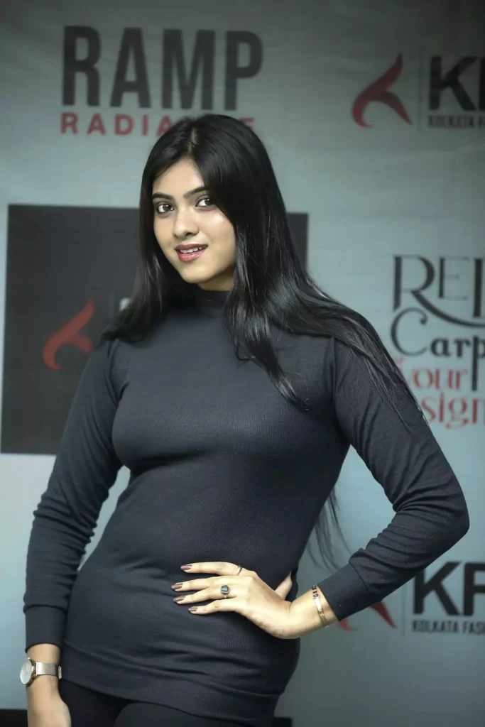Woman in black dress with hand on hip, standing at red carpet event