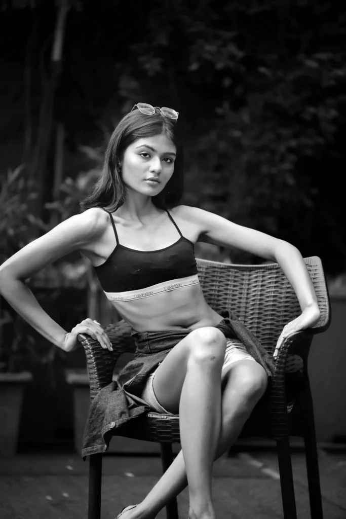 Grayscale photo of fashion-forward woman sitting with one hand on waist