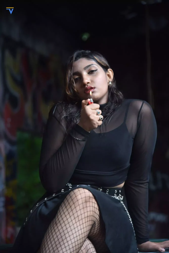 Edgy female model posing with hand raised in front of graffiti wall.