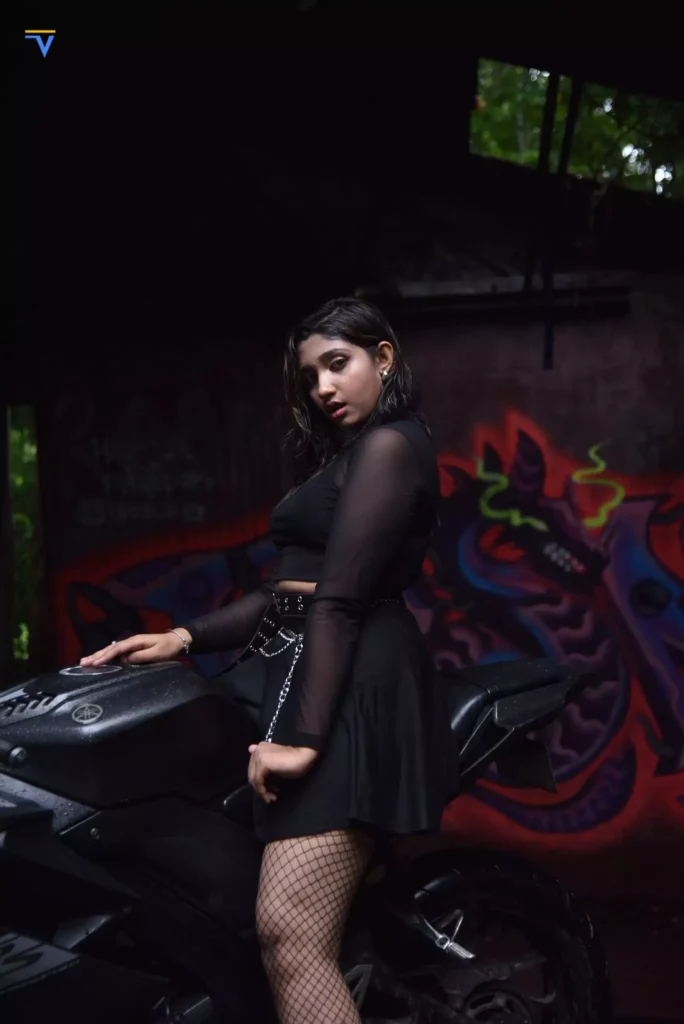 Side profile of bold urban model in black outfit with motorbike and art wall.