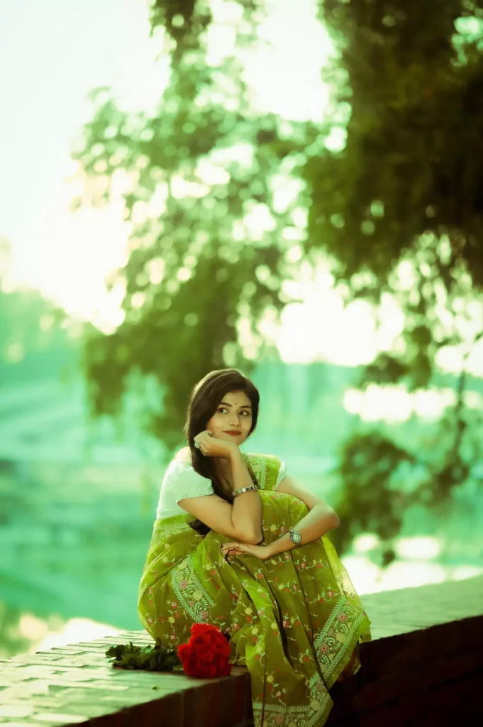 Woman in green saree sitting on a ledge in soft light.