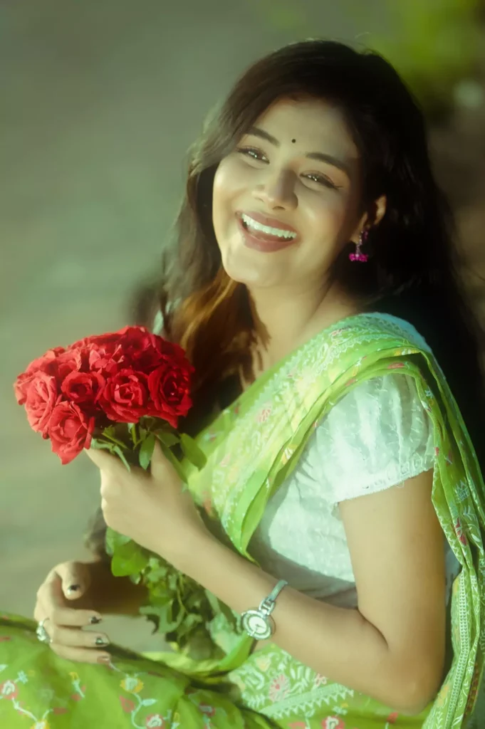 Woman in green saree laughing with flowers.