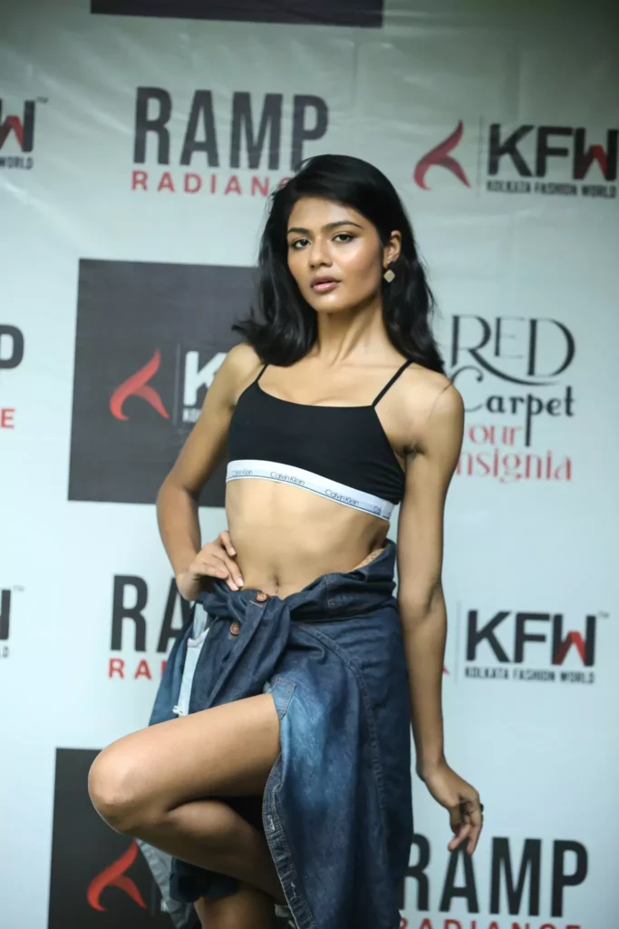 Female model striking confident ramp pose in crop top and denim at KFW Radiance.