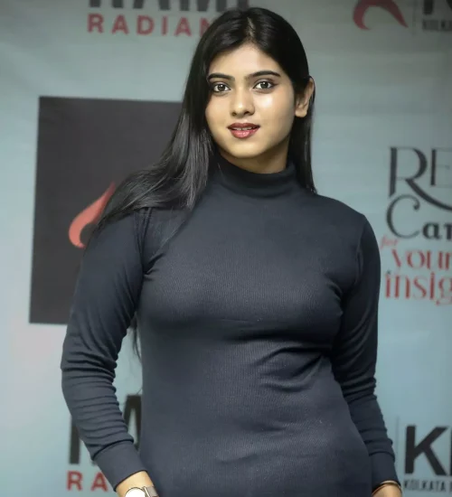 Elegant female model standing straight in black fitted dress with soft smile, in front of fashion event backdrop.